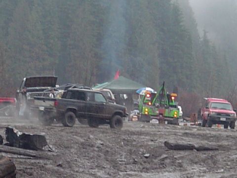 1993 Ford Bronco - Multiple trucks and tow vehicles are gathered in a muddy, outdoor setting.