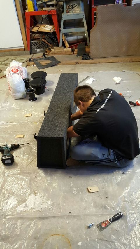 1996 Ford Bronco - A person is assembling a carpeted speaker enclosure in a garage setting with tools and audio equipment present.