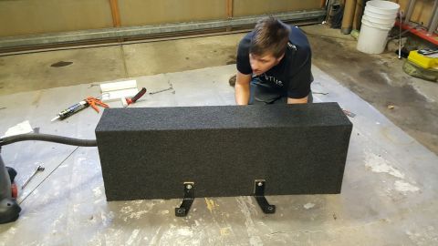 1996 Ford Bronco - A man works on a large, gray subwoofer box in a garage setting.