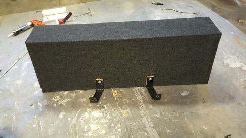 1996 Ford Bronco - A carpeted subwoofer box with two black metal mounting brackets is shown on a concrete floor.