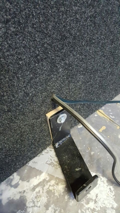 1996 Ford Bronco - A metal bracket is shown attached to a carpeted surface, with a bolt and washer securing it.