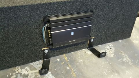 1996 Ford Bronco - A black Alpine car amplifier is mounted to the side of a dark gray, carpeted subwoofer box with black metal brackets and silver bolts. The…
