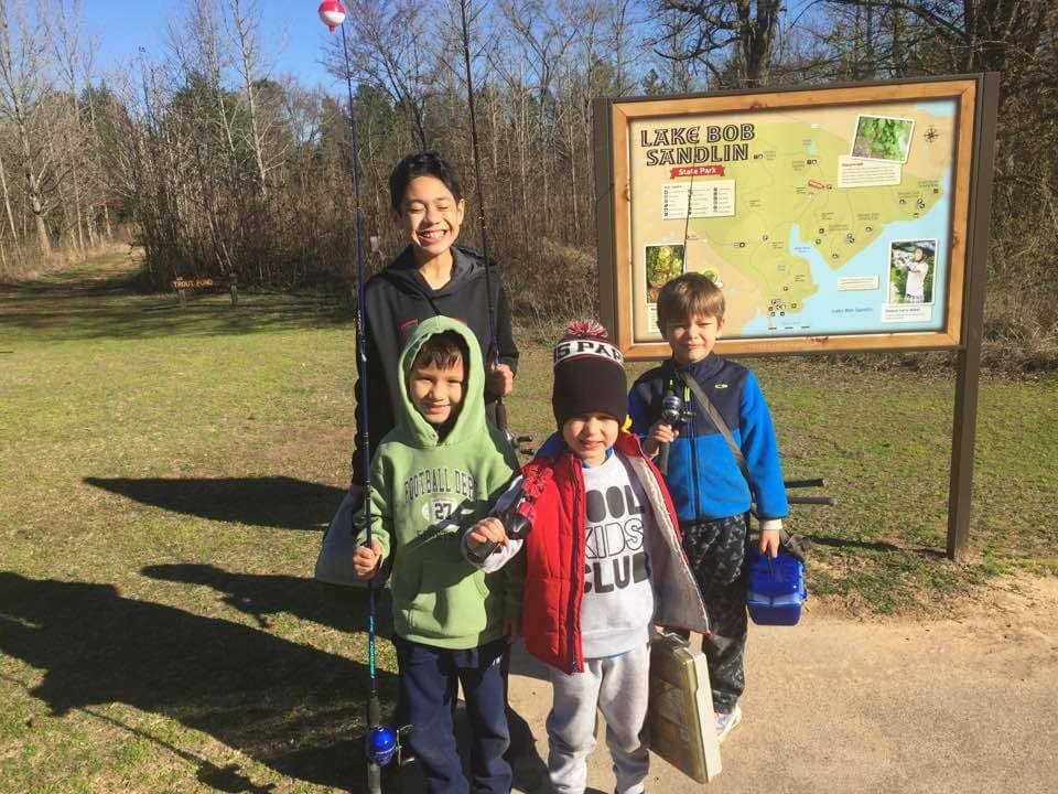 Four boys with fishing rods in front of a park map.