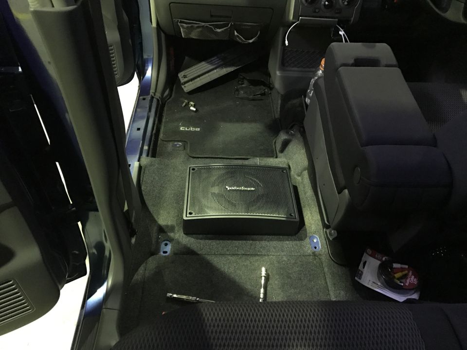 Interior of a car with a subwoofer on the floor and an armrest.