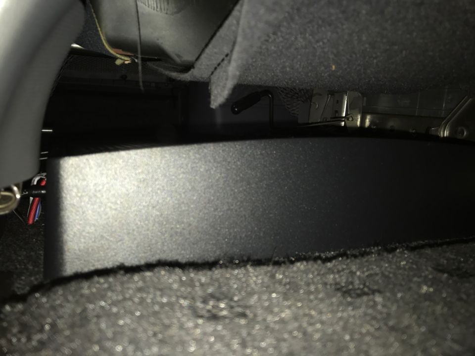 Underside of vehicle seat with black aftermarket enclosure and wires.