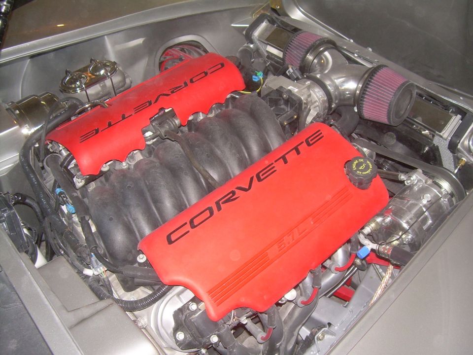 Close-up of a car engine with red Corvette valve covers and dual air intake filters.