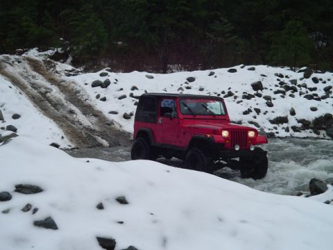 1993 Ford Bronco - A red Jeep Wrangler navigates a shallow, rocky stream covered in snow.