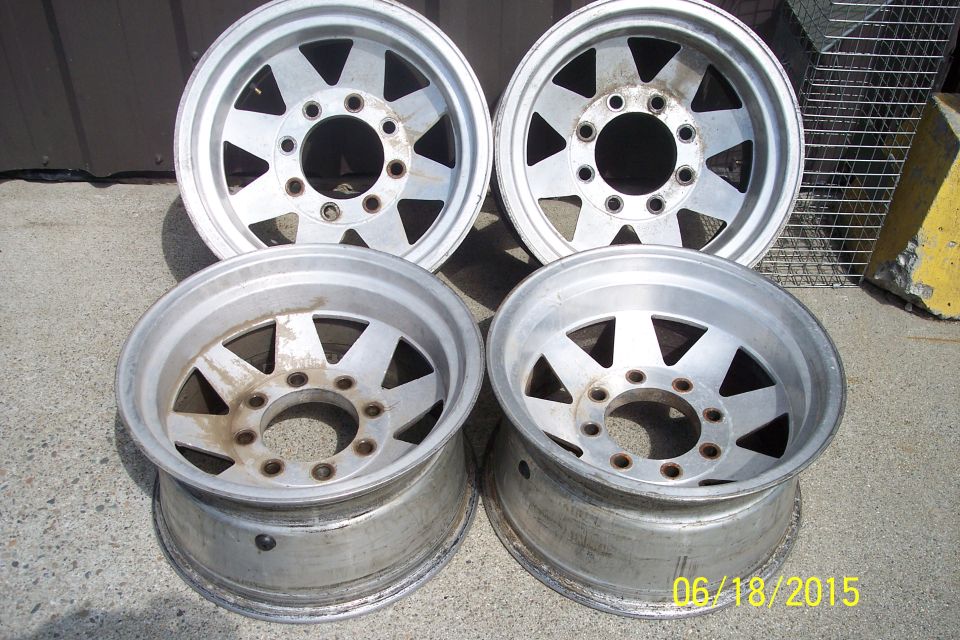 Four aluminum alloy wheels with triangular cutouts on a concrete surface.