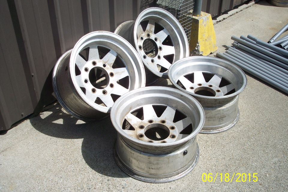 Four aluminum alloy wheels with a five-spoke design on a concrete surface.
