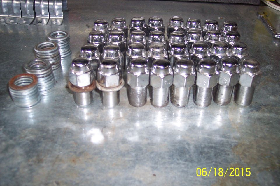 Shiny chrome lug nuts and washers on a metal surface.