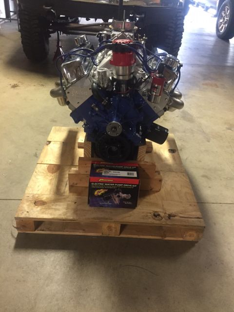 1982 Ford Bronco - A chrome and blue V8 engine is mounted on a wooden pallet in front of a partially visible truck chassis. A box for an electric water pump d…