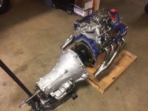 1982 Ford Bronco - A V8 engine and automatic transmission assembly are mounted on a stand and a wooden pallet, ready for installation. The engine features chr…