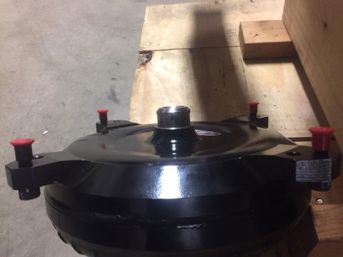 1982 Ford Bronco - A black torque converter with red caps on several mounting bolts is shown in a close-up, angled shot. The part rests on a wooden surface wi…