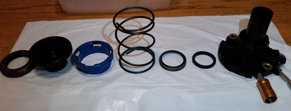Disassembled seal kit parts, springs, O-rings, blue retainer, and black housing laid out on white plastic