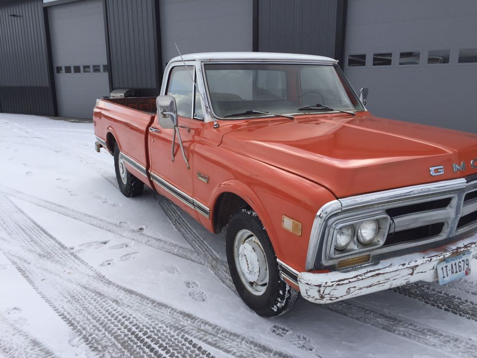Orange GMC pickup truck with white roof in the snow.