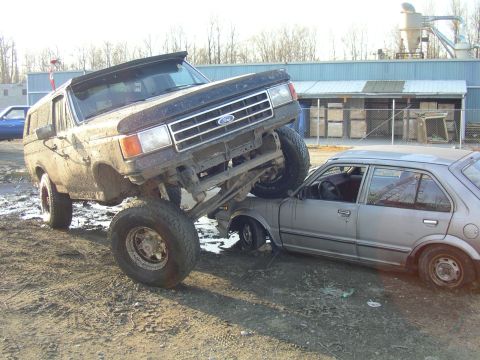 1990 Ford F-150 - Ford Bronco is on top of a sedan, crushing it.