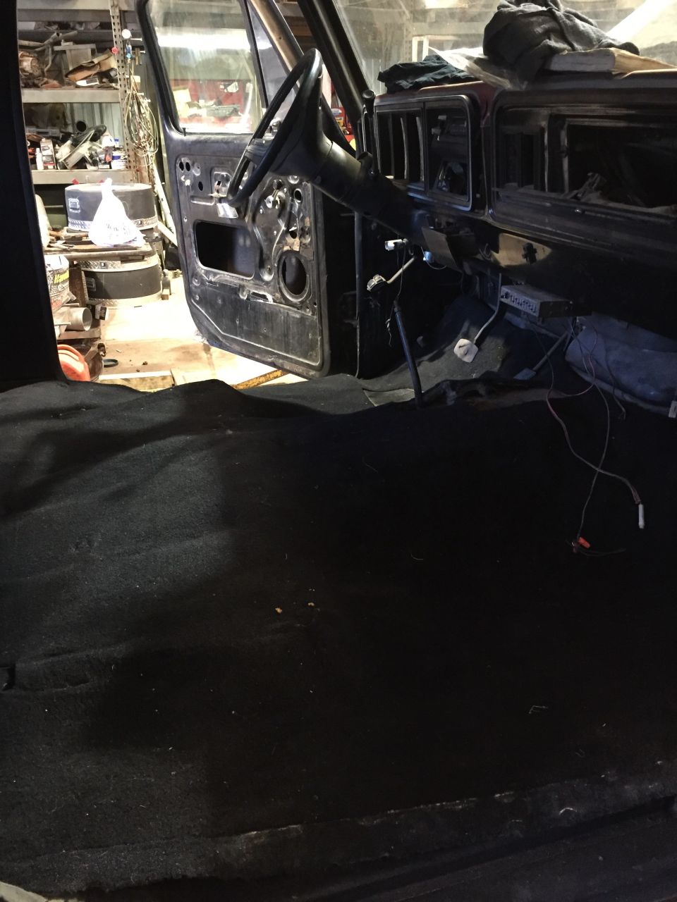 Interior of a classic truck with open door, dashboard, steering wheel, and exposed wiring.
