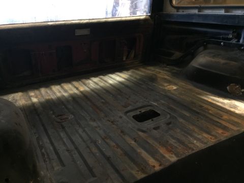 1979 Ford Bronco - The interior bed of a vintage Ford Bronco shows a ribbed metal floor with visible rust and a central square cutout. The rear window is visi…