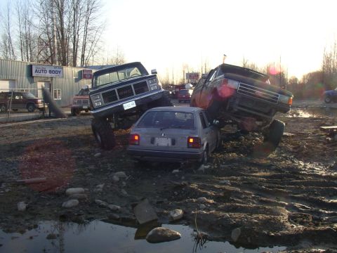 1990 Ford F-150 - Two monster trucks are shown crushing a small car in a muddy, outdoor scene. The registry claims it is a 1990 Ford F-150, but this is not e…