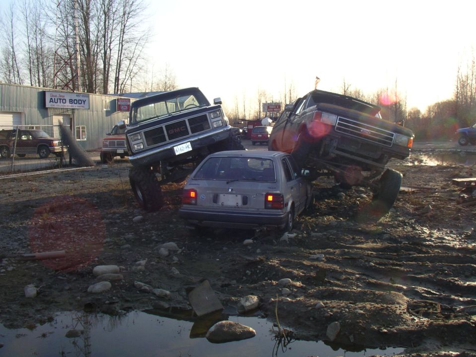 Monster trucks crushing a small car in a muddy lot