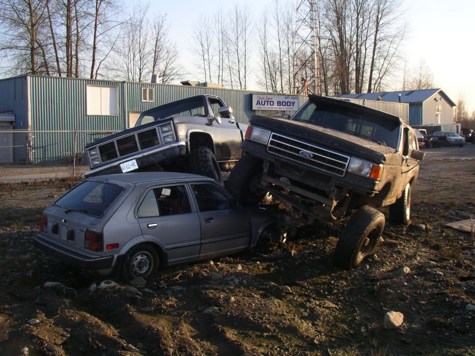 1990 Ford F-150 front 3/4 view, lifted and crushing a car