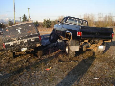 1990 Ford F-150 - Two lifted trucks are stuck in the mud, with one truck resting on top of the other.