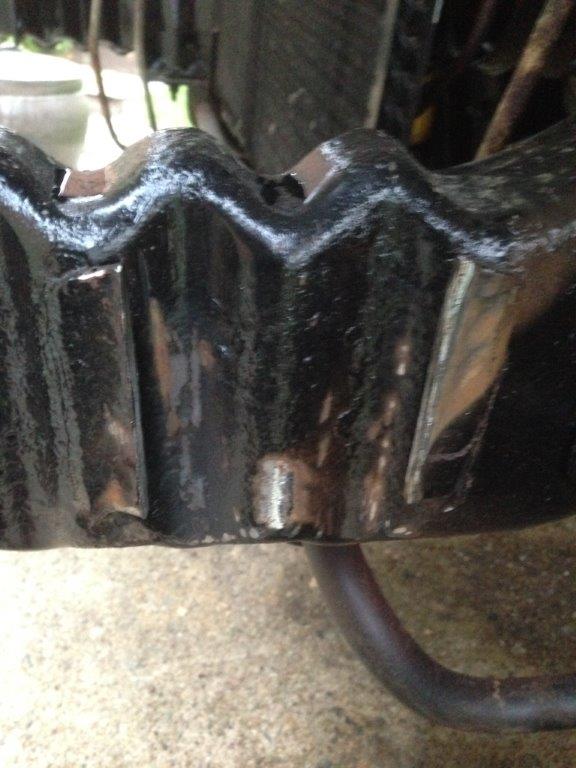 Underside of a black, wavy metal vehicle component with visible wear and a curved pipe.