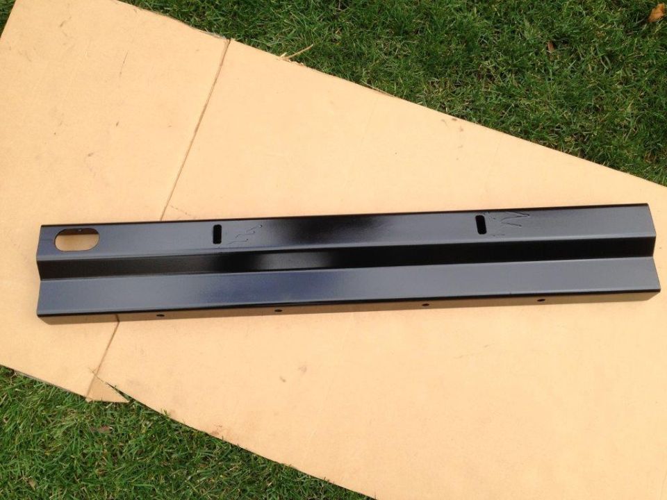 Black metal automotive part with holes and stamped markings.