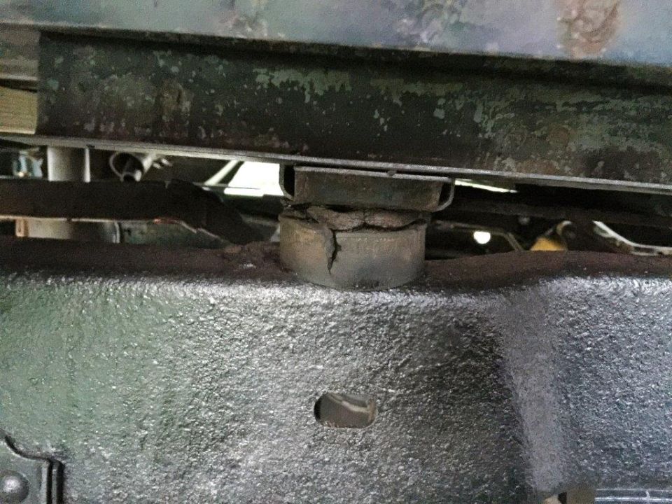 Cracked rubber body mount between a black textured vehicle frame and the underside of the vehicle body.