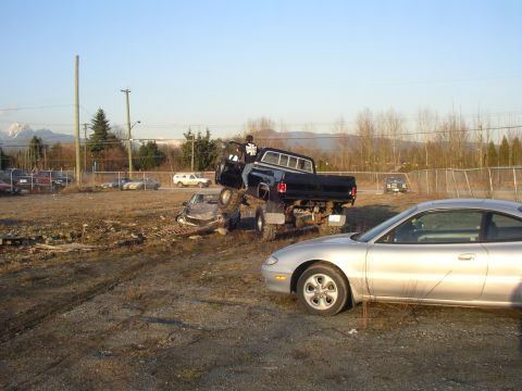 1990 Ford F-150 - This black pickup truck is crushing a car. A silver coupe is parked nearby.