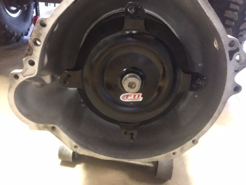 1982 Ford Bronco - A black FTI torque converter is mounted inside the bell housing of a transmission. The torque converter has a red and white FTI decal on it…