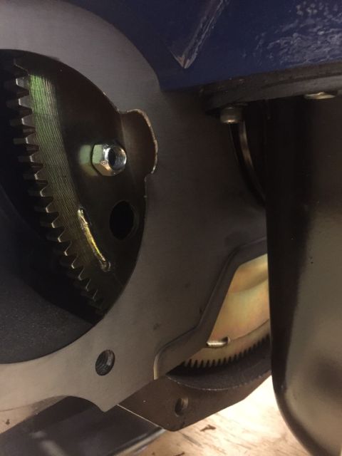 1982 Ford Bronco - A close-up view shows the toothed edge of a flywheel or flexplate assembly, secured by a hex nut and bolt. A portion of a blue painted meta…