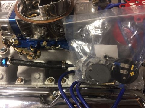 1982 Ford Bronco - Close-up view of a Holley carburetor and engine components, including a black fuel line with blue fittings and a plastic bag containing sma…