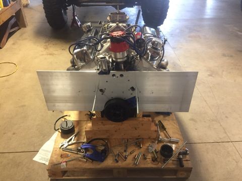 1982 Ford Bronco - A vehicle engine is mounted on a wooden pallet with various tools and parts scattered around it. A large, flat piece of aluminum is attache…