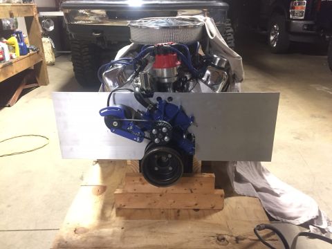 1982 Ford Bronco - A V8 engine with a blue serpentine belt system is mounted on a wooden stand in a garage. The engine is partially covered by a light-colored…