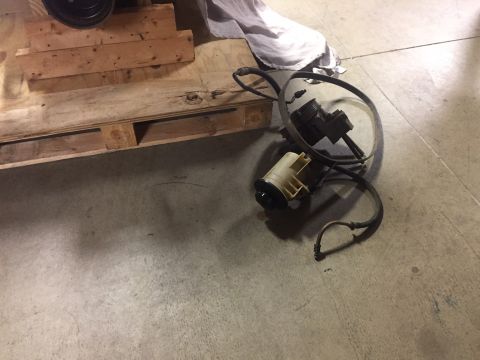 1982 Ford Bronco - A power steering pump and reservoir assembly with hoses is shown resting on a concrete floor next to a wooden pallet.