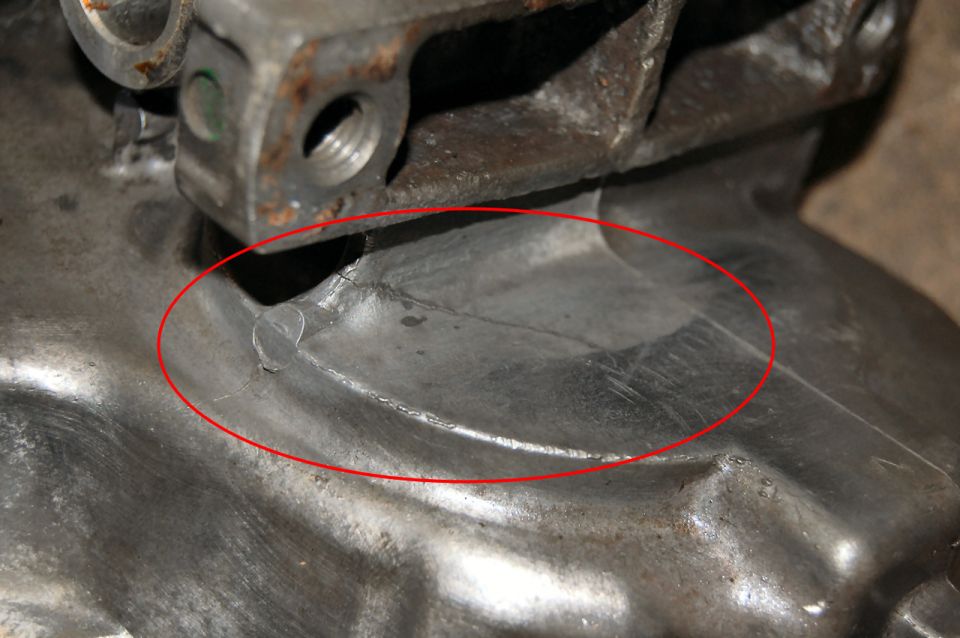 Close-up of a cracked metal component, possibly an engine or transmission housing, highlighted by a red ellipse.