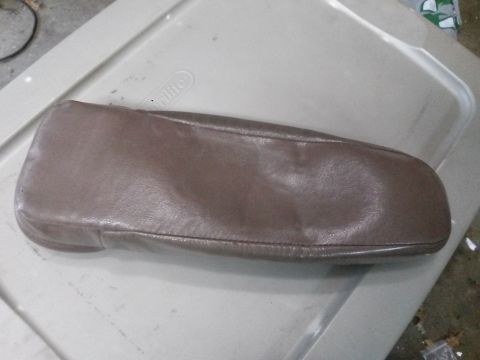 1996 Ford Bronco - A brown leather armrest or console cover is shown resting on a beige plastic storage bin lid. The cover appears to be for a vehicle interio…