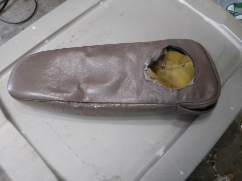 1996 Ford Bronco - A damaged, taupe-colored armrest with a large tear revealing yellow padding is shown resting on a white plastic storage bin.