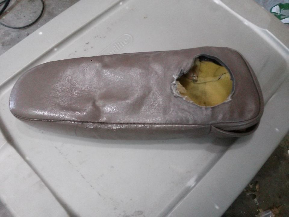 Damaged taupe armrest with a hole in it, resting on a white plastic bin.