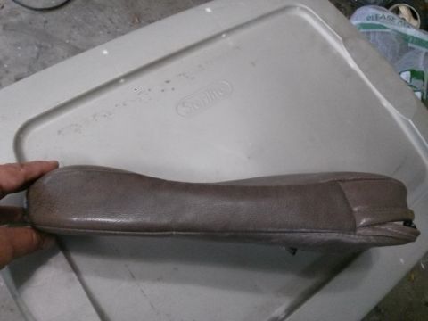 1996 Ford Bronco - A brown leather armrest is shown resting on a tan plastic storage bin lid. The armrest has visible stitching and appears to be slightly wor…