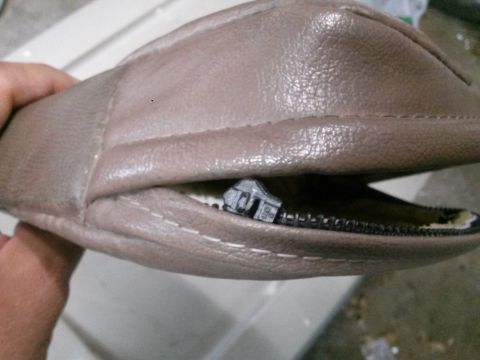 1996 Ford Bronco - A hand holds open a beige zippered pouch, revealing a small gray building with a zipper pull attached.