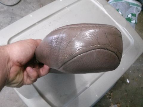 1996 Ford Bronco - A hand holds a brown leather armrest with visible cracking and stitching. The armrest rests on a light-colored plastic storage bin.