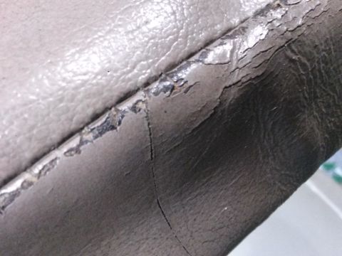 1996 Ford Bronco - Close-up of cracked and peeling faux leather upholstery on a vehicle seat. The material is a light beige color with dark gray undertones vi…