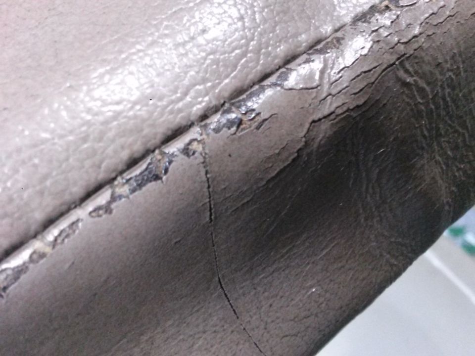 Cracked and peeling beige faux leather upholstery on a vehicle seat.