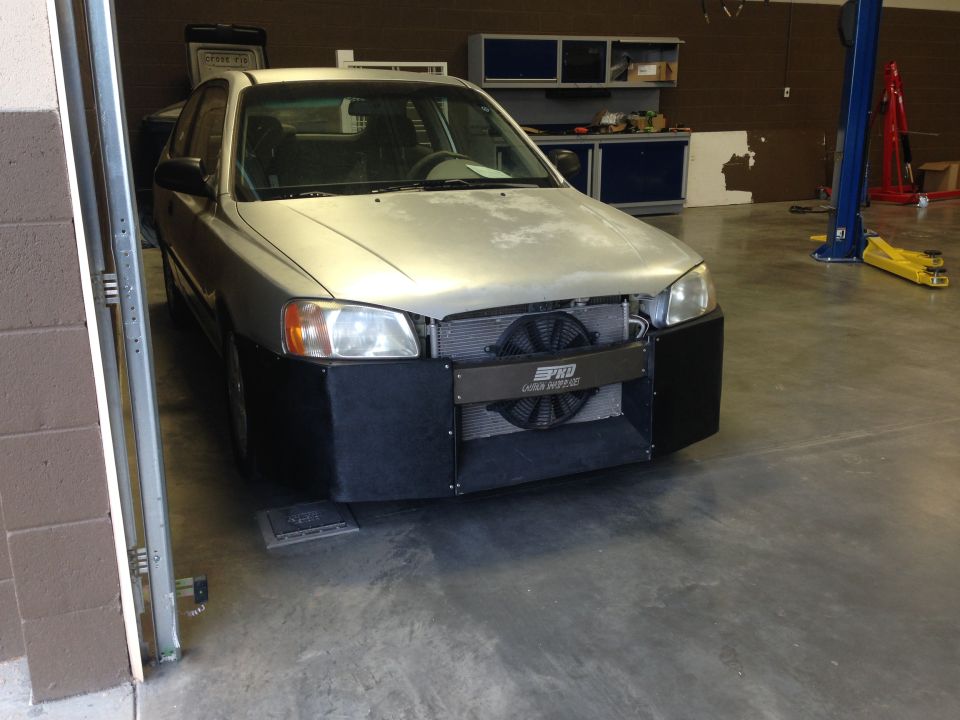 Silver sedan with custom front bumper and exposed radiator fan in a garage.
