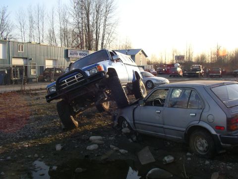 1990 Ford F-150 - Off-road truck crushing a sedan in front of an auto body shop.
