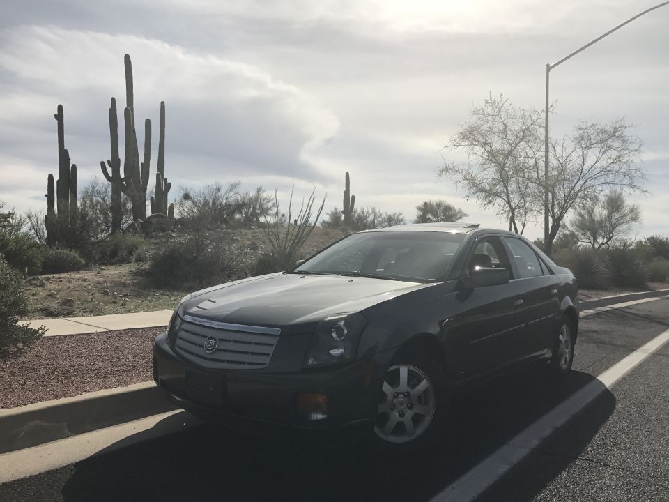 Dark sedan parked on desert roadside with saguaro cacti.