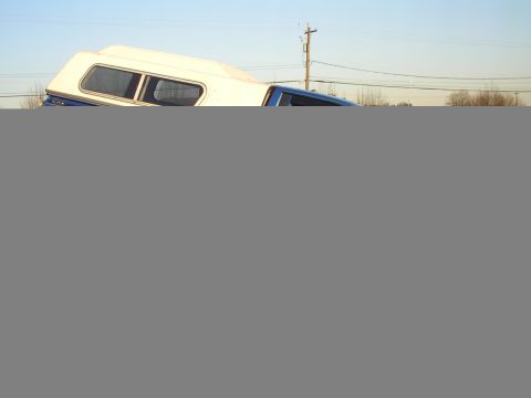 1990 Ford F-150 - A blue pickup truck is fitted with a white camper shell, parked outdoors under a clear sky.