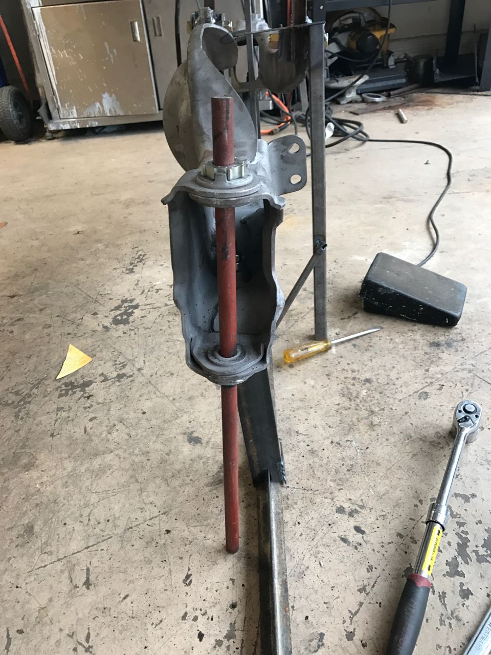 Suspension part with red rod and metal bracket, on a concrete floor with tools